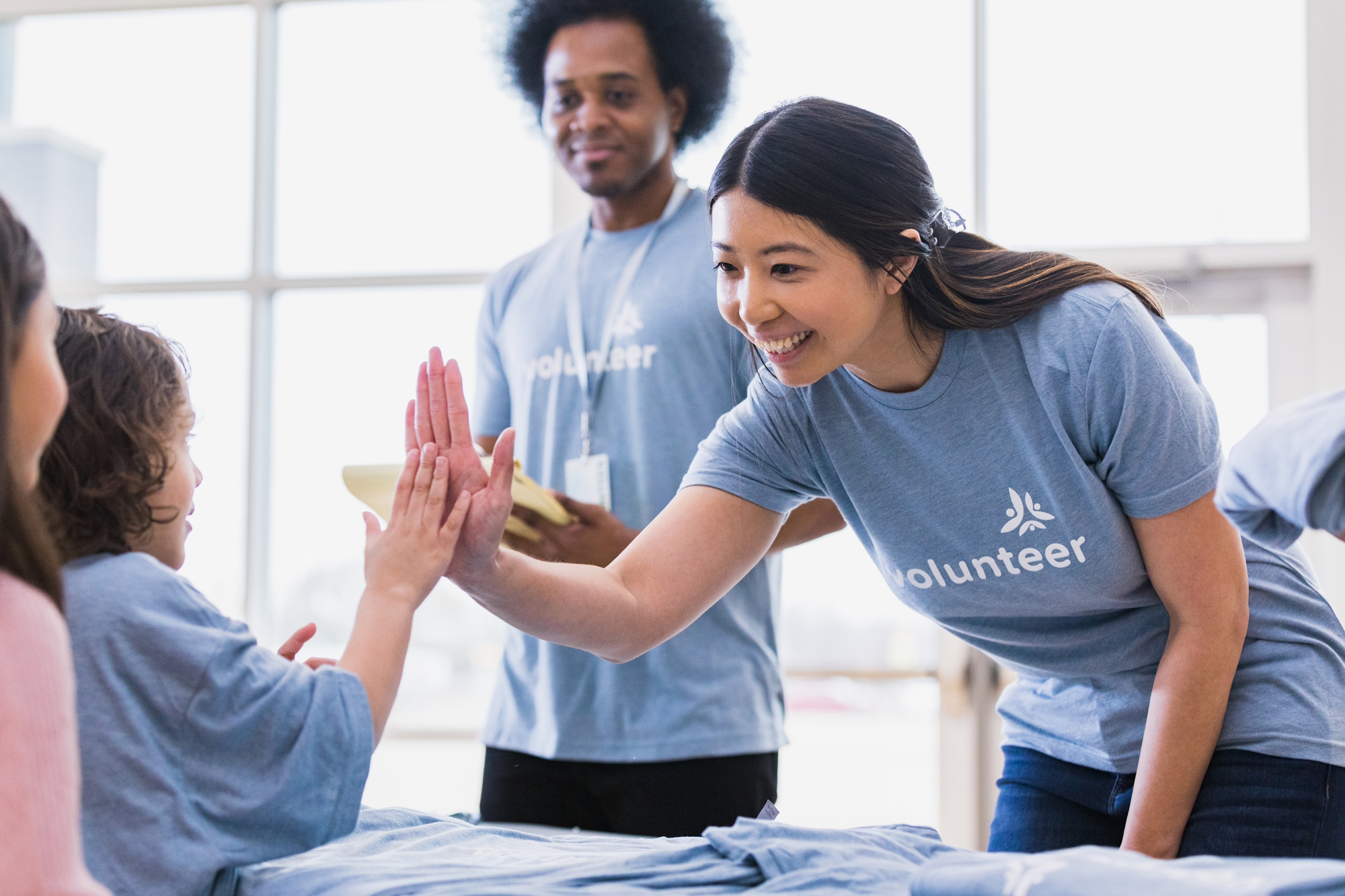 The young adult volunteer welcomes a young child volunteer with a high five and a smile.